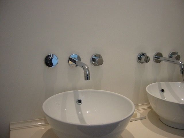 Detailfoto van twee witte ronde waskommen met kranen uit de muur erboven.