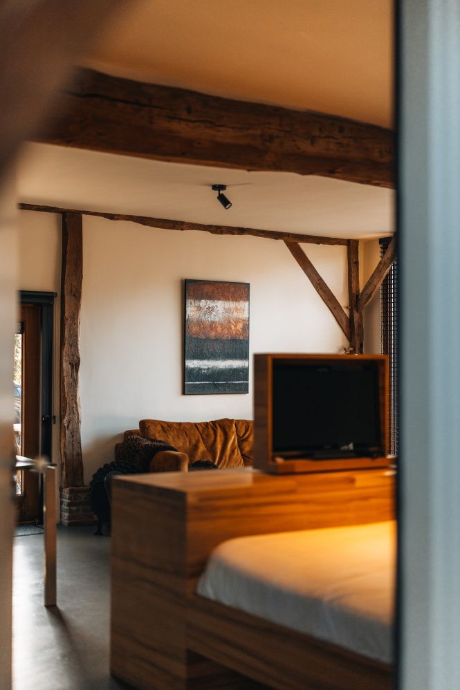 Innenaufnahme eines B&B mit einem Teil des Bettes im Vordergrund und einem gemütlichen Sofa sowie den alten Holzbalken des Bauernhauses im Hintergrund.