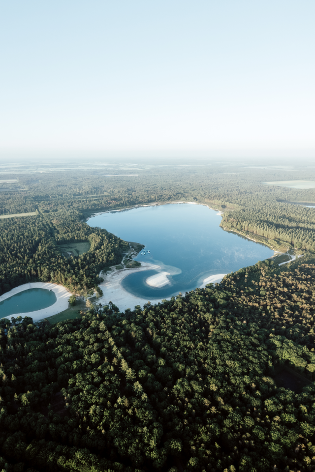 Een dronefoto van het blauwe water van de meren Gasselterveld en 't Nije Hemelrieke, omringd door een groen dicht bos.