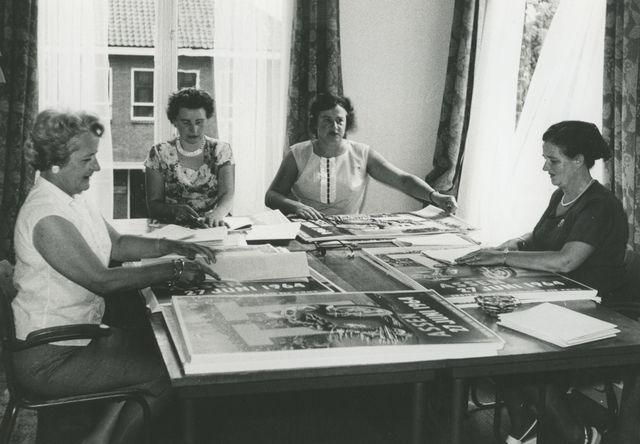 Voorafgaande aan de TT van 1964 wordt de verspreiding van o.a. posters voorbereid op het TT-bureau aan de Torenlaan te Assen. Rechts zit mevrouw Weggemans. De overige personen zijn niet bekend.