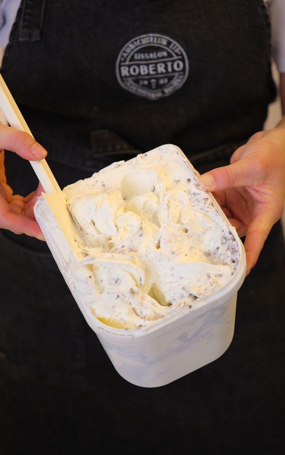 Bak zelfgemaakt ijs bij IJssalon Roberto in Oudewater, vastgehouden door een persoon met een zwart schort aan met daarop het logo van IJssalon Roberto