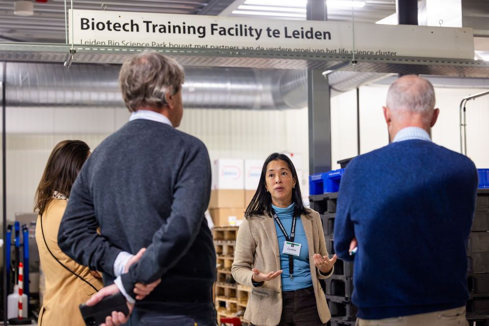 Een groep mensen luistert naar de uitleg van een vrouw bij het Biotech Training Facility te Leiden.