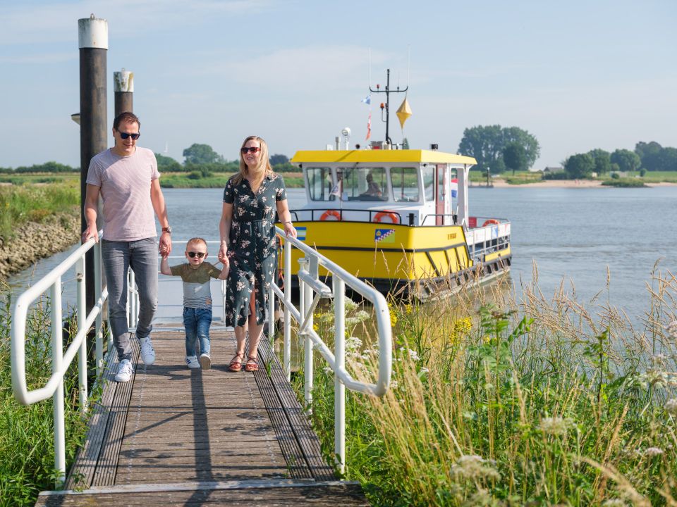 Een vader, kindje en moeder lopen hand in hand over een brug, op de achtergrond staat een geel pondje.