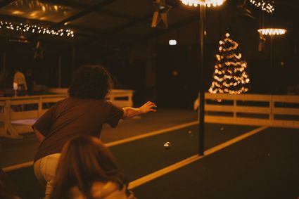 Sfeervolle indoor jeu-de-boulesbaan bij Boerderij De Boerinn, met speler die een bal werpt en warme kerstverlichting op de achtergrond – gezellige winteractiviteit in het Groene Hart.