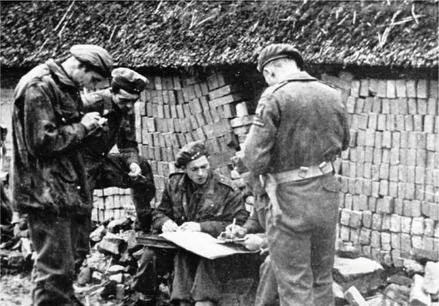 A British paratrooper (as seen from behind), who crossed the river, consults with Polish paratroopers.