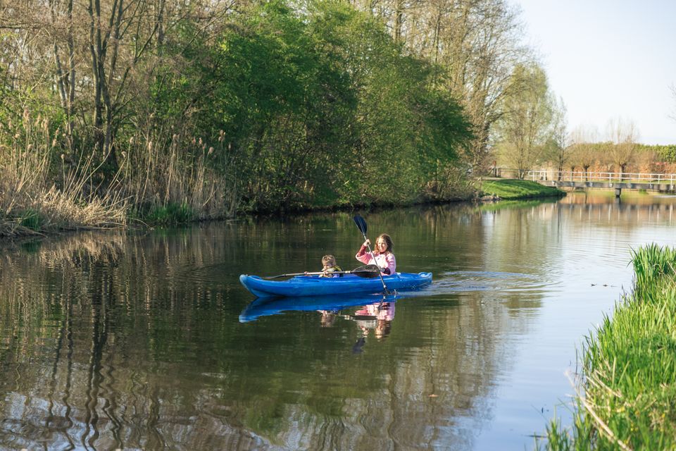 Kind en moeder peddelen met een blauwe kano over de Grebbelinie in Scherpenzeel