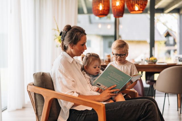 Eine Frau liest zwei Kindern in einem Ferienhaus in Drenthe aus einem Buch vor.