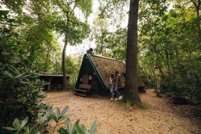 Twee mensen lopen langs ene oude plaggenhut in het Veenpark.