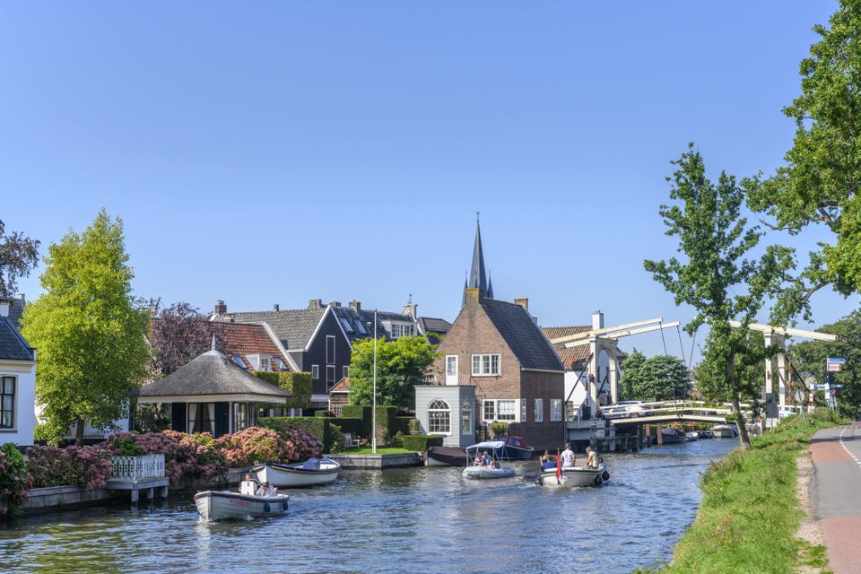 Zicht op de historische kern van Breukelen aan de Vecht met het iconische witte bruggetje van Breukelen en drie varende sloepen op de voorgrond.