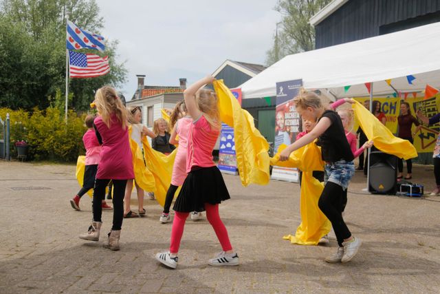 een groep meiden die aan het dansen is met een gele laken.