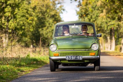 Twee mensen rijden in een DAF van Solexverhuur Friesland door het bosrijke Gaasterland in de herfst.