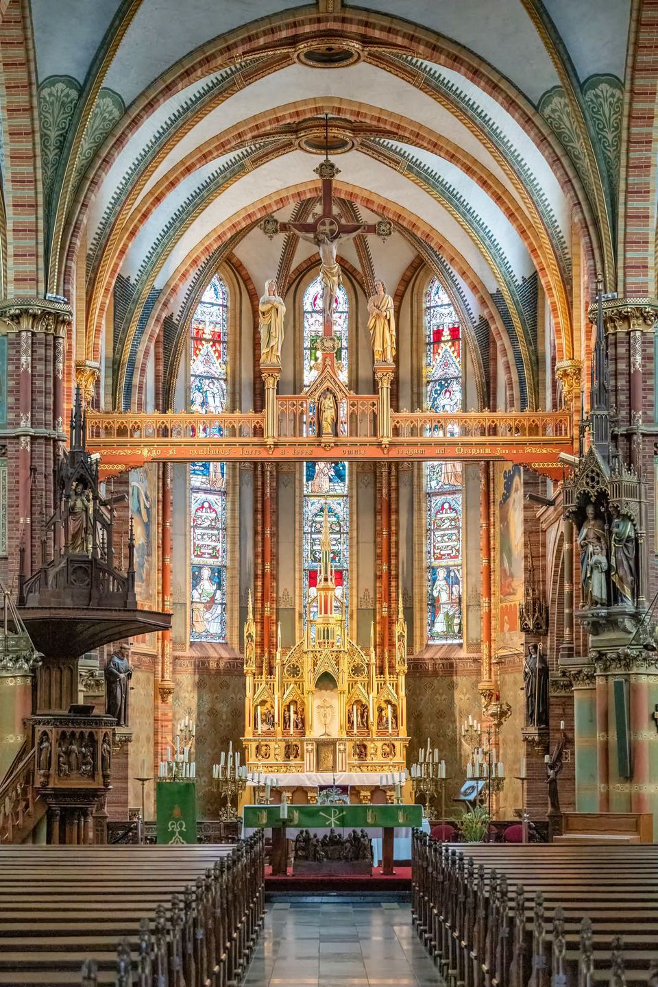 Kerkinterieur van de Sint-Franciscuskerk in Oudewater, Groene Hart. Neogotische katholieke kerk met rijk versierd hoogaltaar, glas-in-loodramen, kruisbeeld, gewelfde plafonds en symmetrisch zicht vanaf het middenschip.