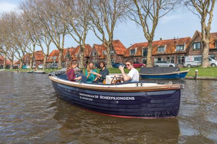 Sloepverhuur De Scheepsjongens in Woerden, Groene Hart, met vier mensen die in een sloep varen langs het Singelwater en karakteristieke woningen.