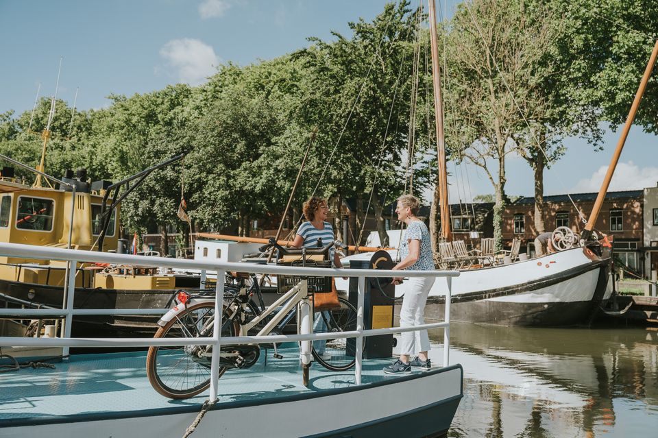 Museumwerf Vreeswijk, regio Utrecht, fietsers op ponton tussen oude boten en erfgoed aan het water tijdens recreatief dagje fietsen langs streekmusea.