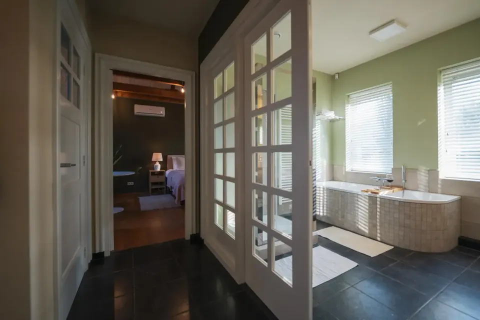 Doorkijkje met aan de rechterkant een lichte badkamer met ligbad en donkere slaapkamer op de achtergrond.