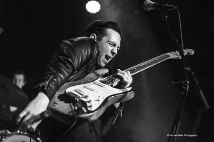 Theaterpodium Het Klooster, Woerden, Groene Hart, zwart-wit concertfoto van gitarist met elektrische gitaar onder spotlicht tijdens energiek live optreden met microfoon op het podium.