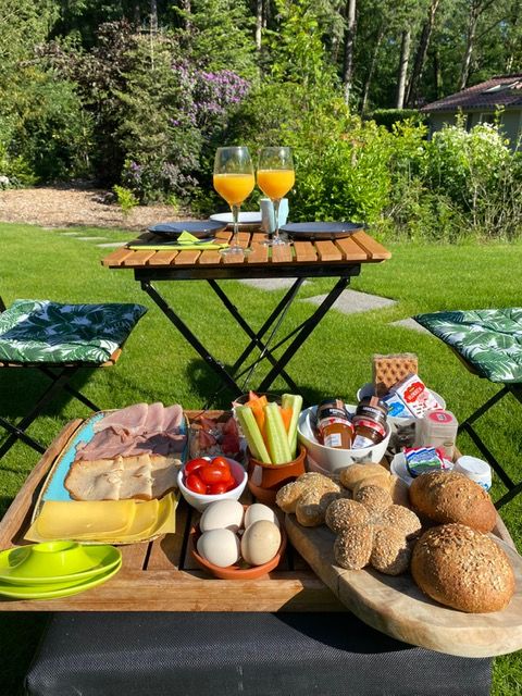 Ontbijt in de bosrijke tuin, met broodjes, beleg, eitjes, rauwkost en glaasjes jus d'orange. Bistrot-zitje.
