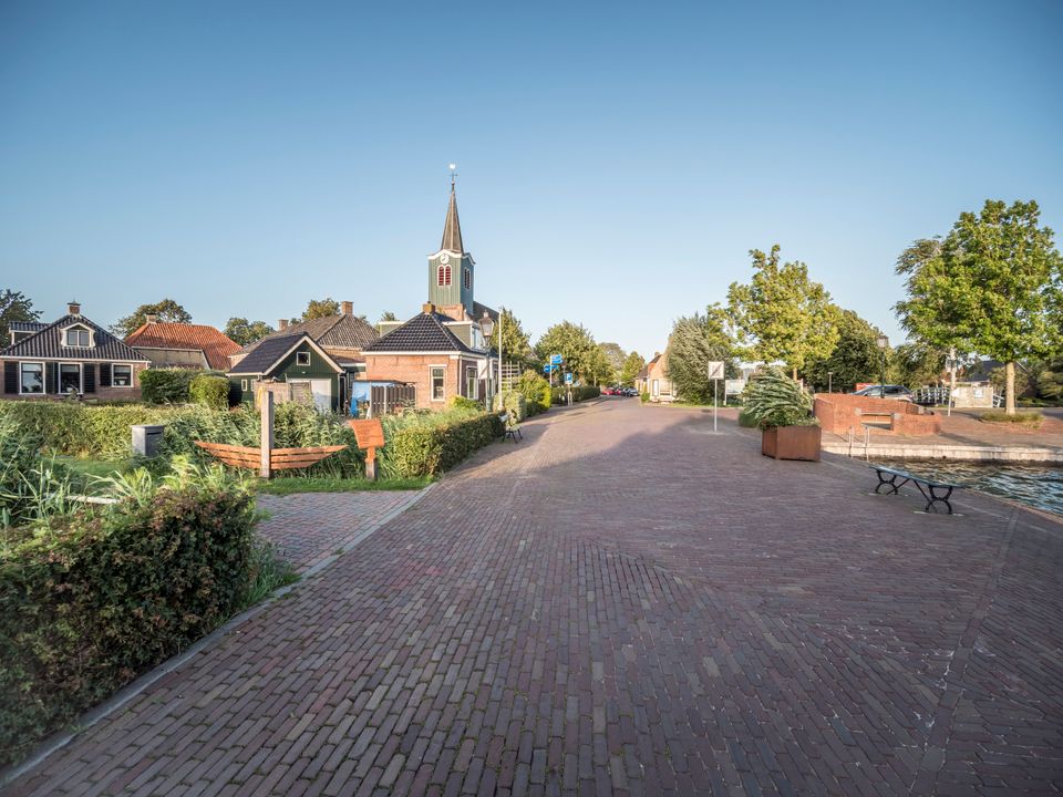 Een foto van het dorpje oudega, de zon valt mooi over de straat en de kerk.