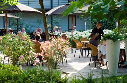 Terras met diverse zitjes, veel groene beplanting en donkere parasols.