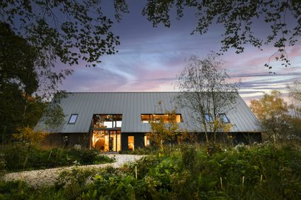 Avondfoto van het hoofdgebouw met verlichte ingang in een groene omgeving en een blauw-paarse lucht.