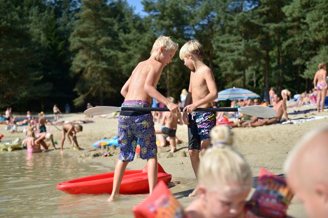 Kinderen spelen op een zomerse dag aan de waterrand van een Drentse zwemplas midden in de Drentse natuur.