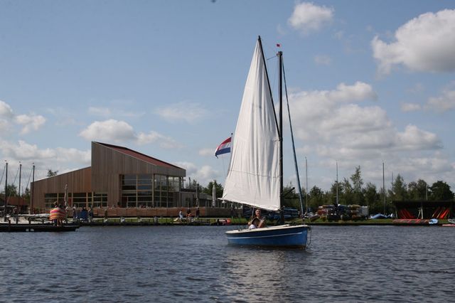 Ein Segelboot fährt über das Wasser vorbei an einem Pavillon.