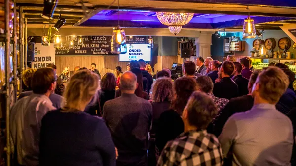een publiek kijkt naar een podium met een dia getiteld ondernemerscafé