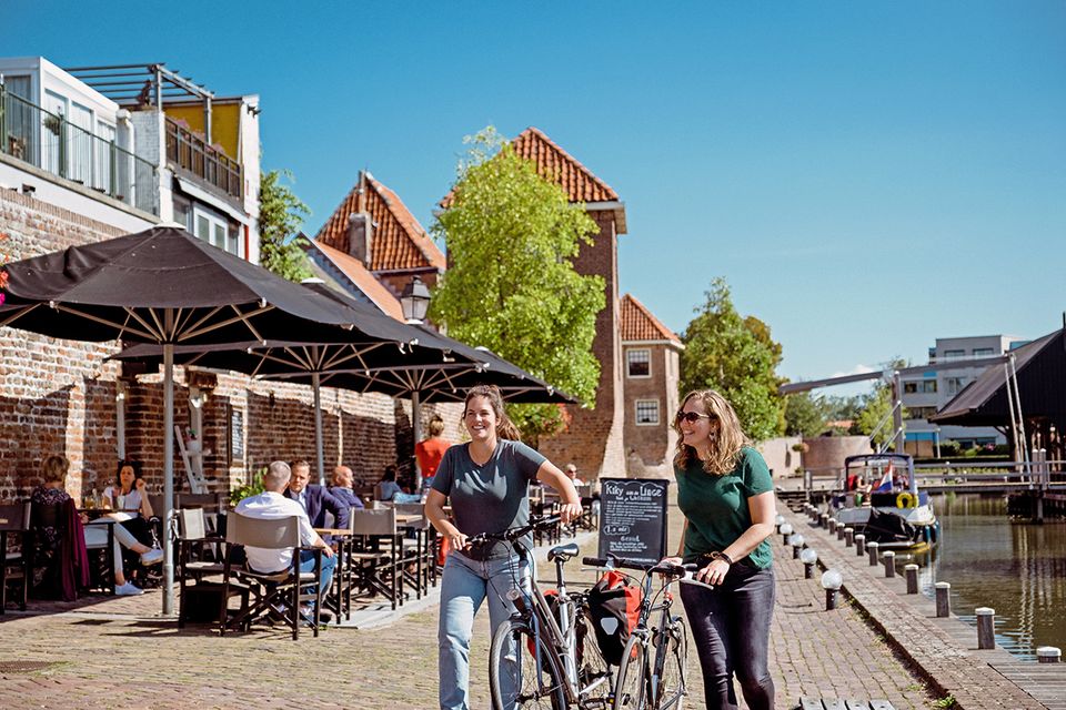 Fietsers genieten van een tussenstop op een terras aan de historische haven van Leerdam in het Groene Hart. Een recreatieve fietstocht langs het water combineert cultuur, horeca en ontspannen genieten in de vestingstad.