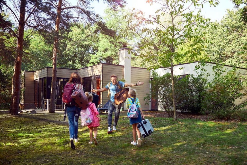 Eine Familie geht mit ihren Taschen und Koffern zu einem Ferienhaus.