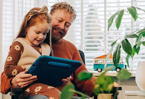 kind bij vader op schoot met een ipad in de hand