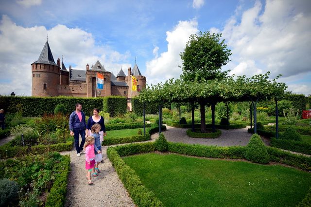 Gezin loopt in de kasteeltuin met het Muiderslot op de achtergrond.
