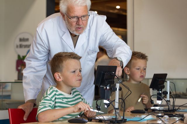 Schelpenexpert Hans Post helpt twee kinderen met wat er te zien is op hun microscoop