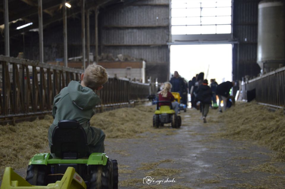 Kinderen die op speelgoed tractors rijden door de stallen van boerderij Hardebol