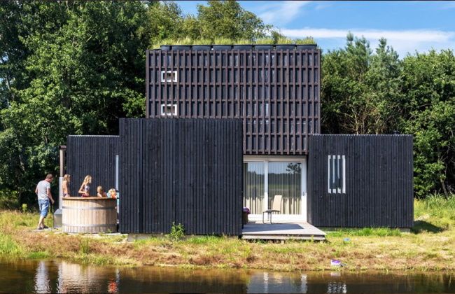 Overnachtingsaccommodatie met een huttub ernaast met natuur er omheen en een vijver voor de accommodatie.