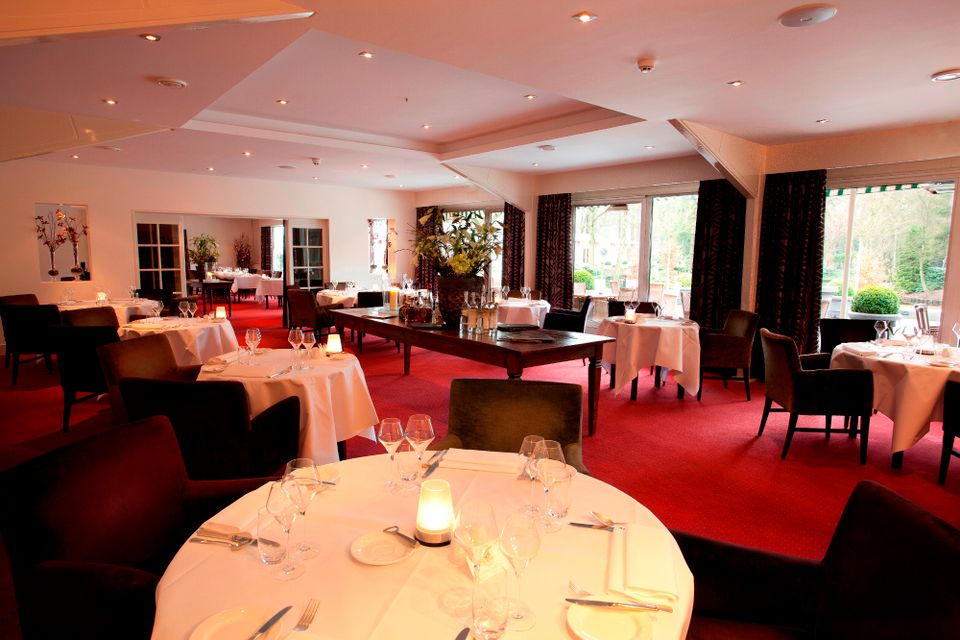 Het restaurant met diverse ingedekte tafel op rode vloerbedekking.