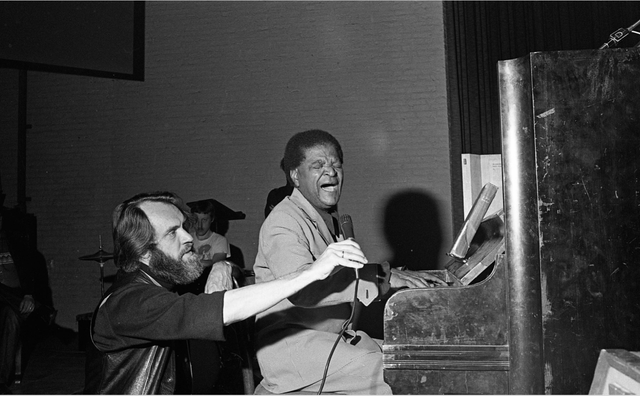Vrijwilliger Jazz in Duketown houdt microfoon vast voor de artiest in 1976