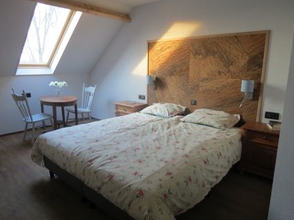 Witte slaapkamer met dakraam met daaronder een zitje en een twee-persoonsbed tegen een houten paneel.