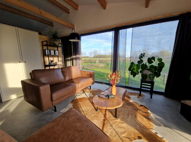 Woonkamer met bruine bank, koeienvel op de vloer, een houten salontafeltje en uitzicht op het platteland.