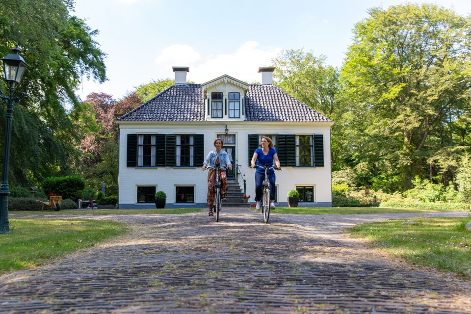 Twee vrouwen fietsen weg van een monumentaal pand.