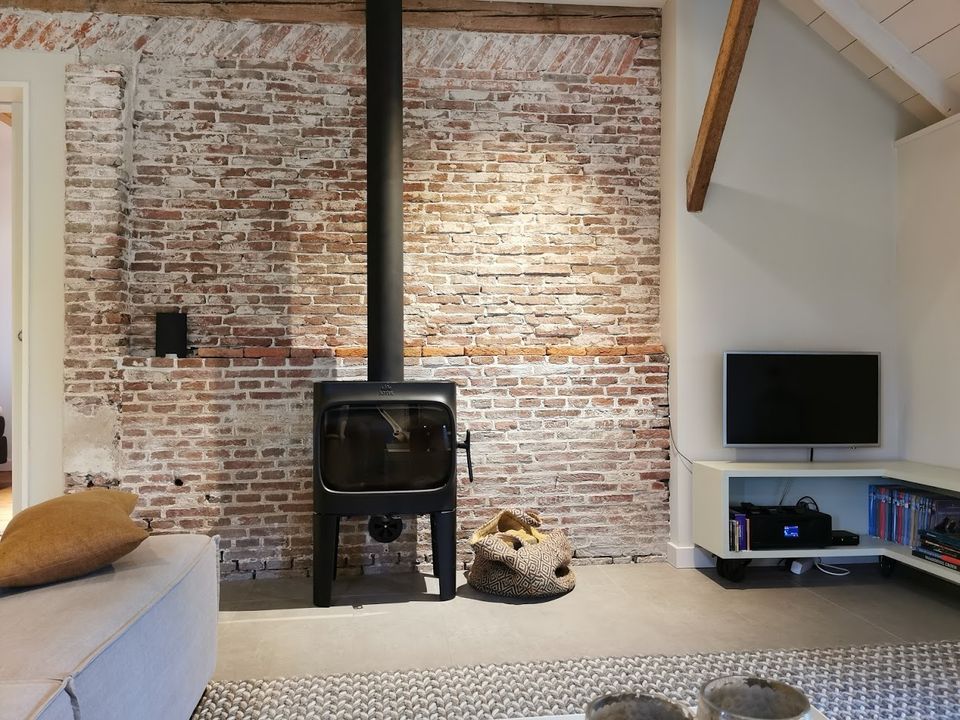 Interieur van Natuurhuisje Elsehof Logies met een sfeervolle houtkachel tegen een robuuste bakstenen muur en een warme, landelijke inrichting.