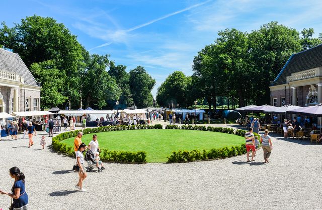 Overzicht van de trotsmarkt bij kasteel groeneveld. Het gras is groen, er staan kraampjes en de zon schijnt.