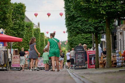 Winkelende mensen in de Midstraat van Joure. Er staan reclameborden op de straat en er hangen lampions in de lucht.