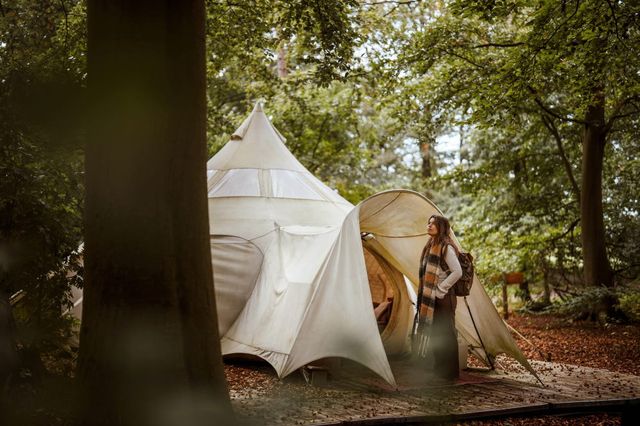 Een vrouw staat bij een tent in de natuur op een camping in Drenthe.