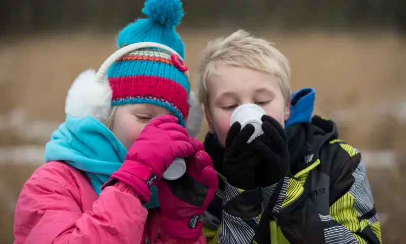 Twee kinderen die warm aangekleed zijn, drinken uit een beker.
