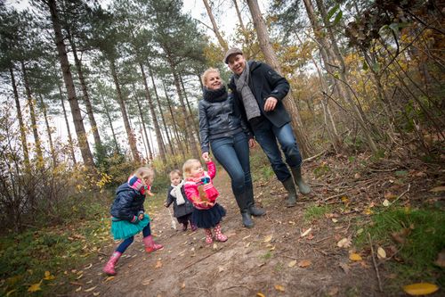 Een gezin met drie kinderen wandelen in de herfst in het bos met kaplaarzen aan.