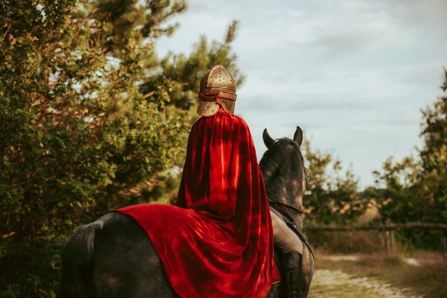 Achteraanzicht roofridder met helm en cape op paard.