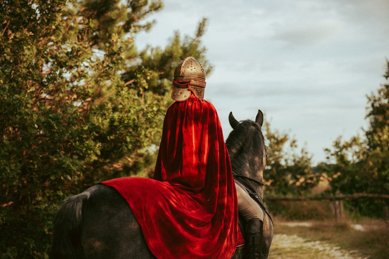 Achteraanzicht roofridder met helm en cape op paard.