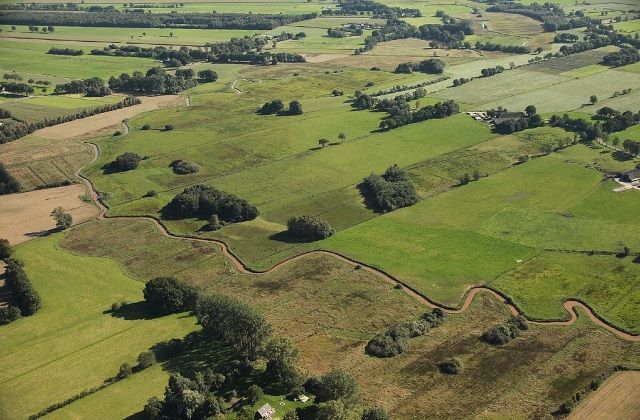 Luchtfoto van groene velden waar rivier de Reest doorheen kronkelt.
