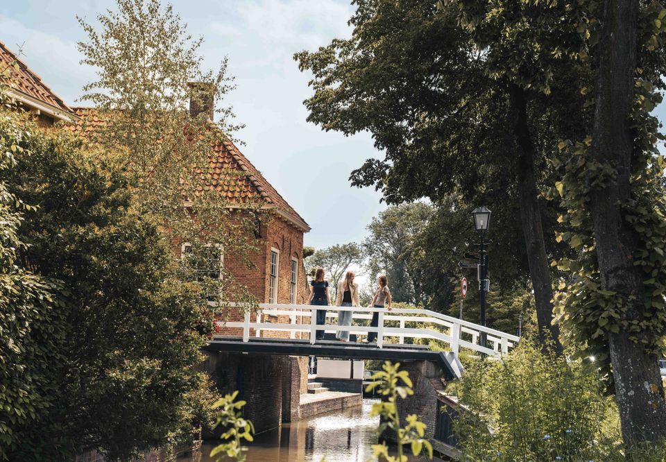 Dorpsbrug in Linschoten, gemeente Montfoort, Groene Hart, met drie wandelaars op een witte brug over het water tussen historische bebouwing en groen.