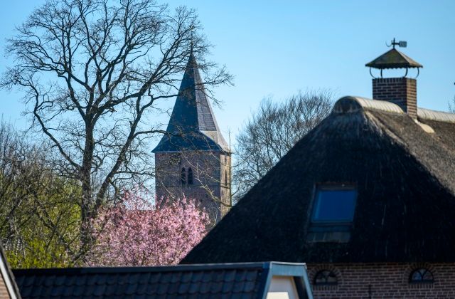 Kerktoren steekt boven een boerderij uit.